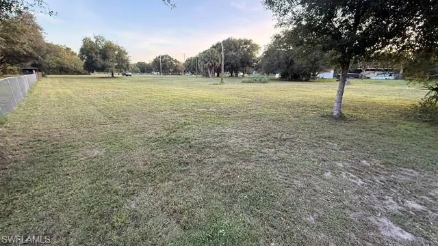Expansive grassy lot featuring mature trees and a chain-link fence boundary