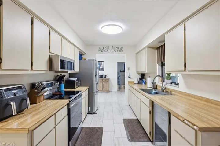 Kitchen with light tile patterned floors, butcher block counters, wine cooler, appliances with stainless steel finishes, and sink