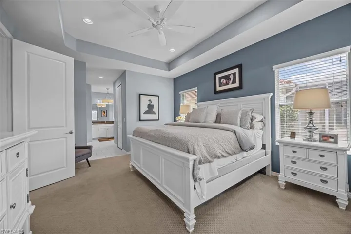 Carpeted bedroom with a tray ceiling, ceiling fan, and ensuite bathroom