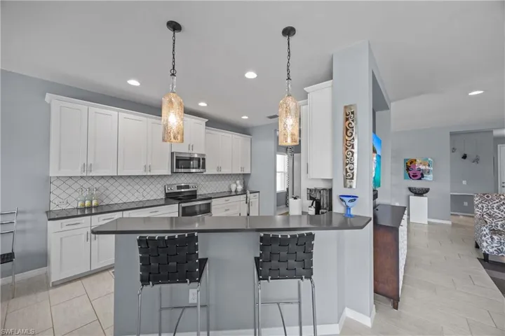 Kitchen with kitchen peninsula, appliances with stainless steel finishes, a kitchen bar, and white cabinets