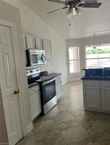 Kitchen featuring stainless steel appliances, lofted ceiling, dark countertops, a ceiling fan, and a textured ceiling