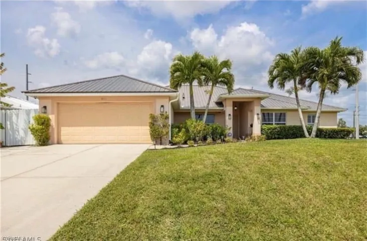 Ranch-style home with stucco siding, a front yard, driveway, an attached garage, and a metal roof