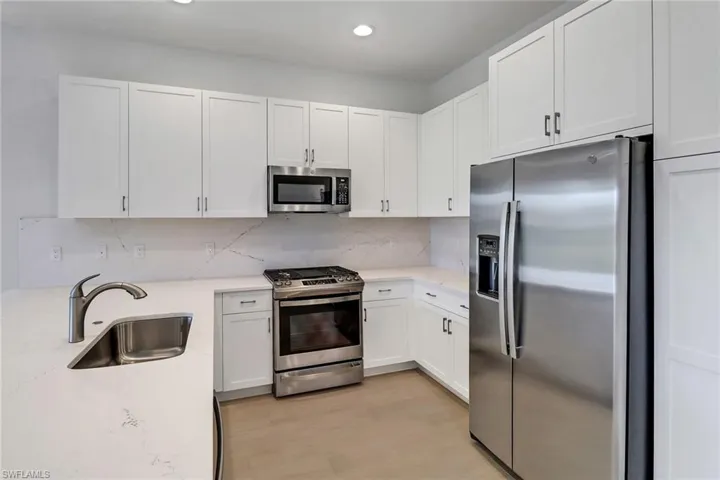 Kitchen with white cabinets, sink, tasteful backsplash, light hardwood / wood-style flooring, and appliances with stainless steel finishes