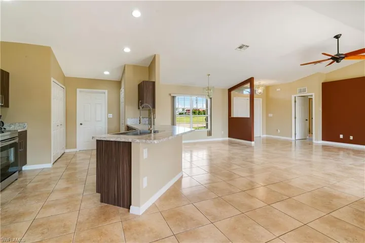Kitchen with sink, a center island with sink, decorative light fixtures, ceiling fan with notable chandelier, and vaulted ceiling