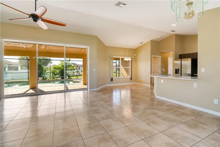 Empty room featuring ceiling fan with notable chandelier, vaulted ceiling, sink, and light tile patterned floors