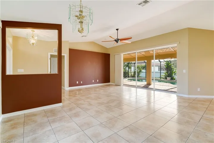 Empty room featuring ceiling fan with notable chandelier, vaulted ceiling, and light tile patterned floors
