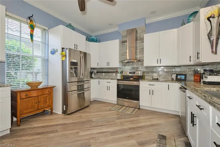 Kitchen featuring stainless steel appliances, decorative backsplash, light wood-type flooring, ceiling fan, and wall chimney exhaust hood
