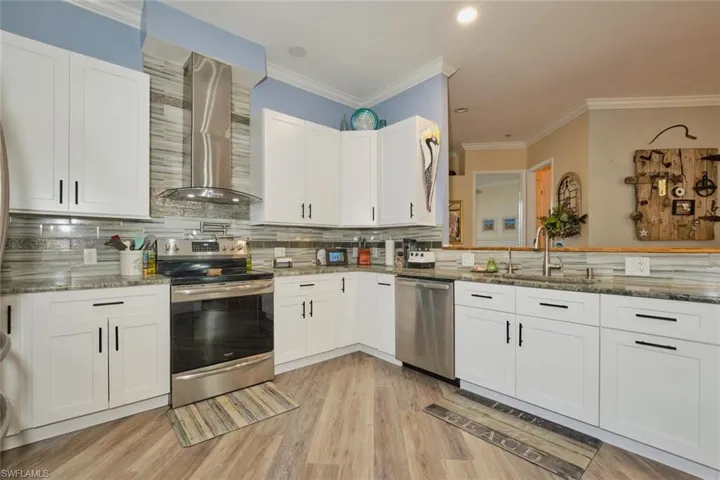 Kitchen with appliances with stainless steel finishes, stone countertops, tasteful backsplash, and wall chimney exhaust hood