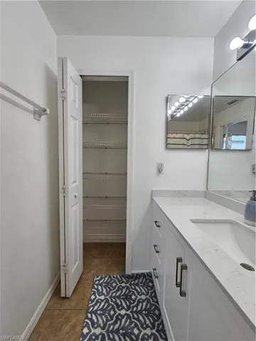 Bathroom featuring a vanity with a white countertop and integrated sink, white cabinetry with metal pulls, and a wall-mounted mirror