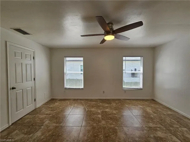 Spacious room featuring tile flooring, two windows with blinds, a ceiling fan with integrated lighting, and a paneled door