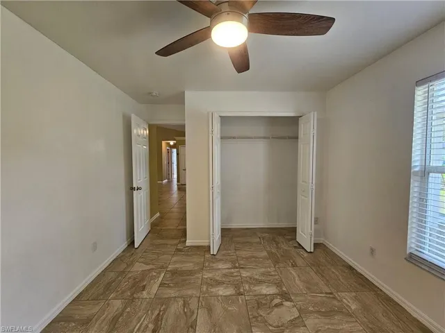 Room featuring tile flooring, a ceiling fan with light fixture, a window with horizontal blinds, and a bi-fold door closet