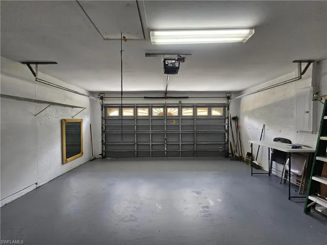 Spacious garage featuring a durable concrete floor, an overhead door with transom-style windows, and a built-in access panel