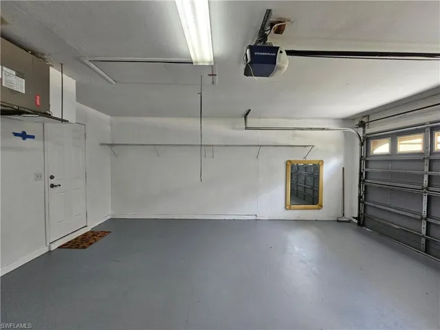 Spacious garage featuring a painted concrete floor, fluorescent ceiling lighting, an automatic garage door opener, and integrated wall shelving