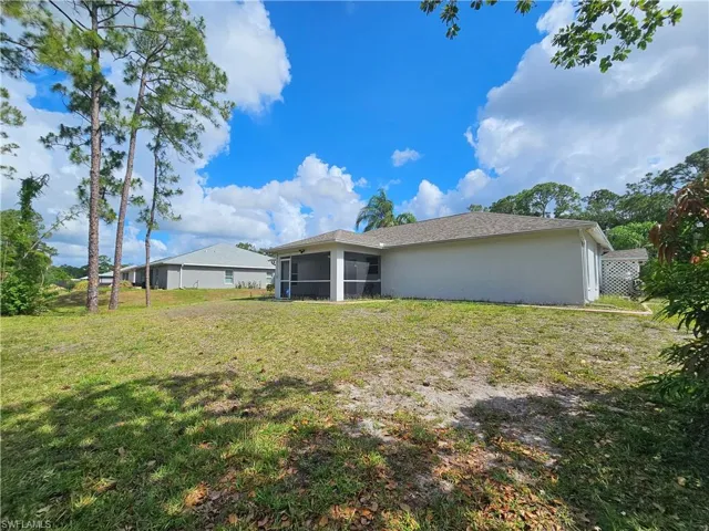 Expansive rear yard featuring mature pine trees, a screened lanai, and a neutral-toned exterior