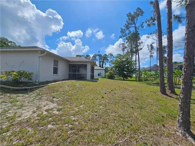 Expansive rear lawn featuring a screened patio, mature trees, and a stucco exterior