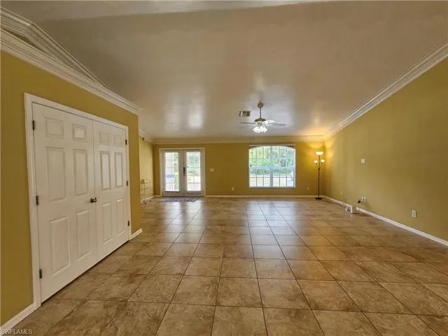 Spacious interior room featuring large format tile flooring, crown molding, double French doors, a ceiling fan with light fixture, and a large arched window