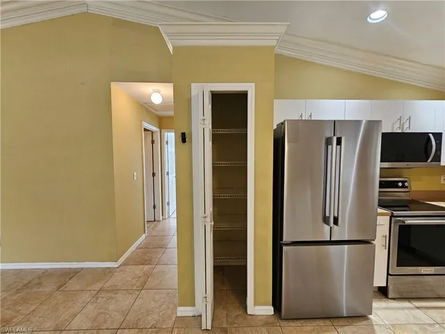 Kitchen area featuring vaulted ceilings with crown molding, stainless steel appliances, white cabinetry, and tile flooring