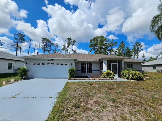 Single-story residence featuring an attached two-car garage, painted driveway, screened front entry, arched window, and mature landscaping