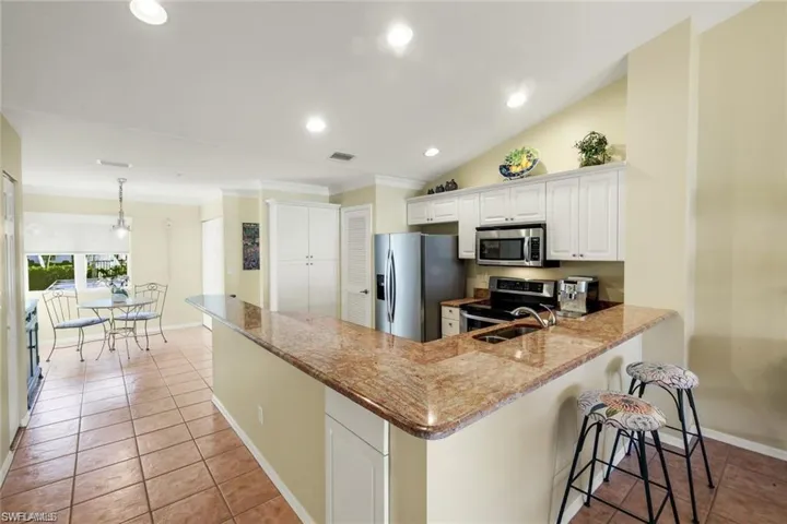 Kitchen with a peninsula, white cabinetry, stainless steel appliances, dark stone countertops, and hanging light fixtures