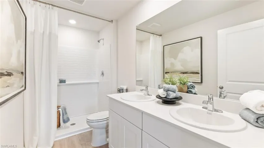 MODEL PHOTO - Full bathroom with curtained shower, double vanity, and light wood-style floors