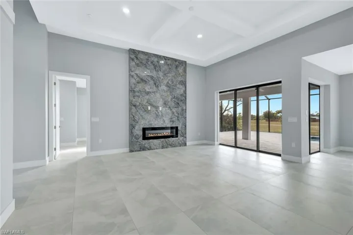 Unfurnished living room with coffered ceiling, a fireplace, a towering ceiling, beamed ceiling, and recessed lighting