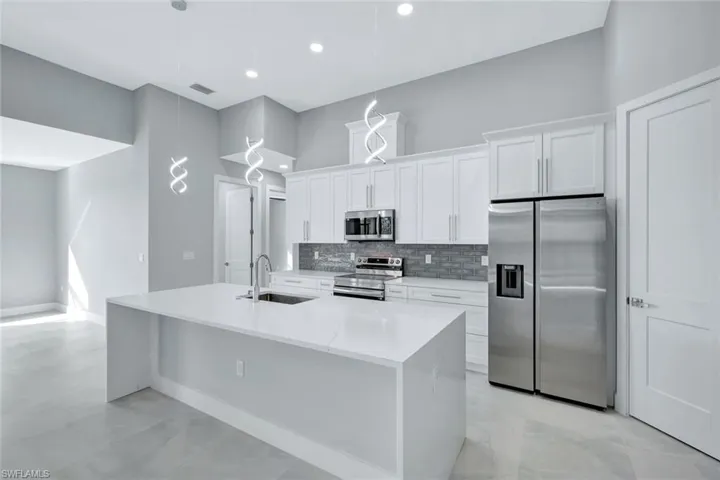 Kitchen featuring stainless steel appliances, light stone countertops, white cabinets, an island with sink, and recessed lighting