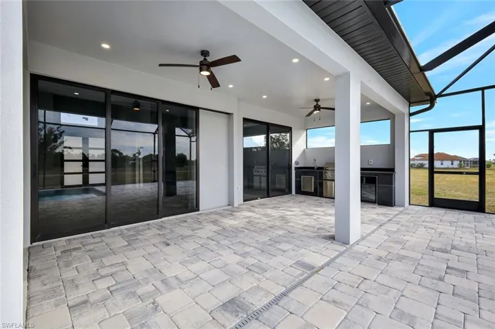 View of patio featuring a lanai, a sunroom, a ceiling fan, and exterior kitchen