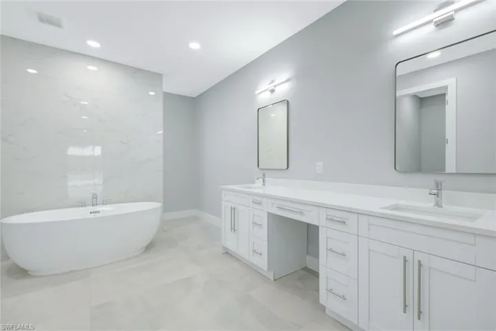 Full bath featuring a freestanding bath, double vanity, recessed lighting, and light marble finish flooring