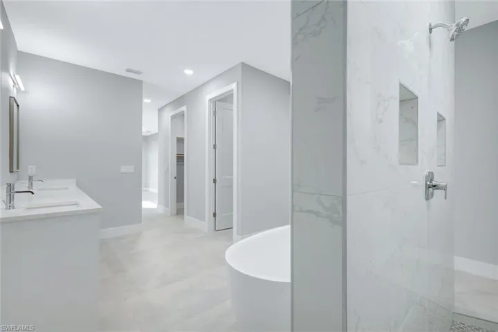 Bathroom with a freestanding tub, double vanity, a marble finish shower, a walk in closet, and recessed lighting