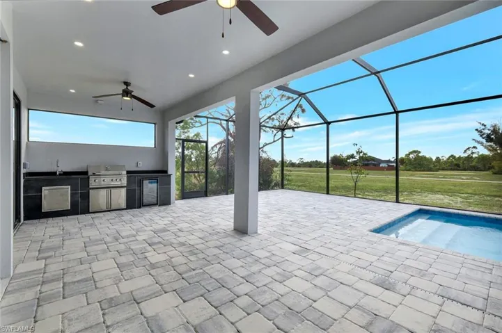 View of patio featuring an outdoor kitchen, a sunroom, a ceiling fan, and glass enclosure