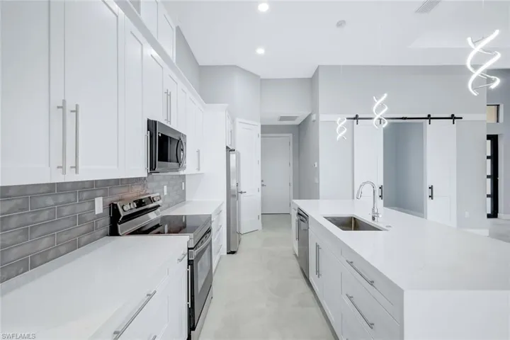 Kitchen with a barn door, appliances with stainless steel finishes, white cabinets, pendant lighting, and light stone countertops