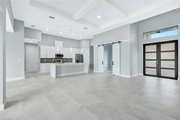 Kitchen featuring a towering ceiling, coffered ceiling, a barn door, open floor plan, and white cabinets