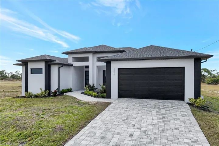 Prairie-style home with stucco siding, decorative driveway, a front yard, and a garage