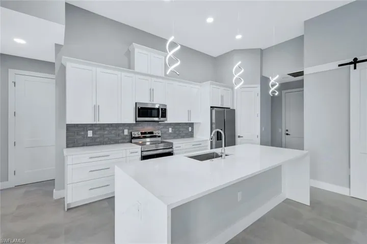 Kitchen with stainless steel appliances, white cabinetry, a barn door, light stone counters, and recessed lighting