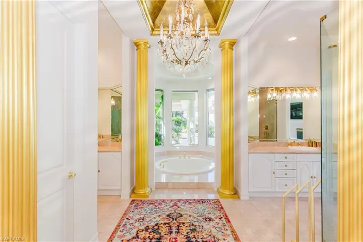 Bathroom featuring tiled bath, vanity, an inviting chandelier, a tray ceiling, and ornate columns