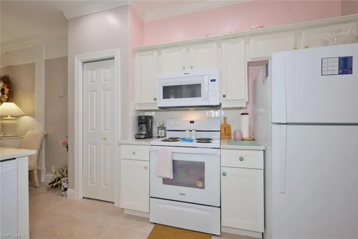 Kitchen featuring tasteful backsplash, ornamental molding, white cabinets, light tile patterned floors, and white appliances