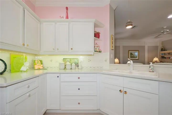 Kitchen featuring decorative backsplash, ornamental molding, sink, white cabinets, and ceiling fan