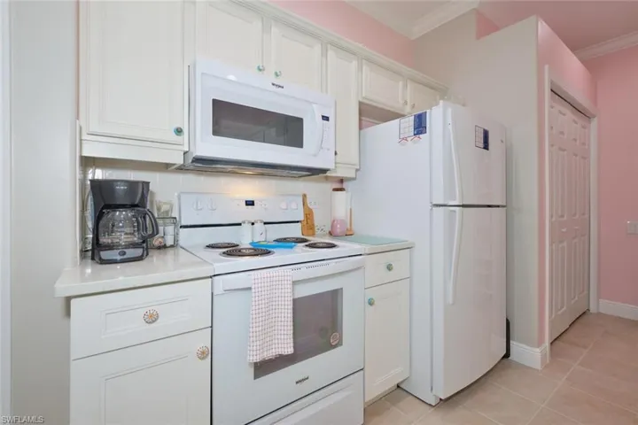Kitchen featuring backsplash, white appliances, white cabinets, and light tile patterned floors