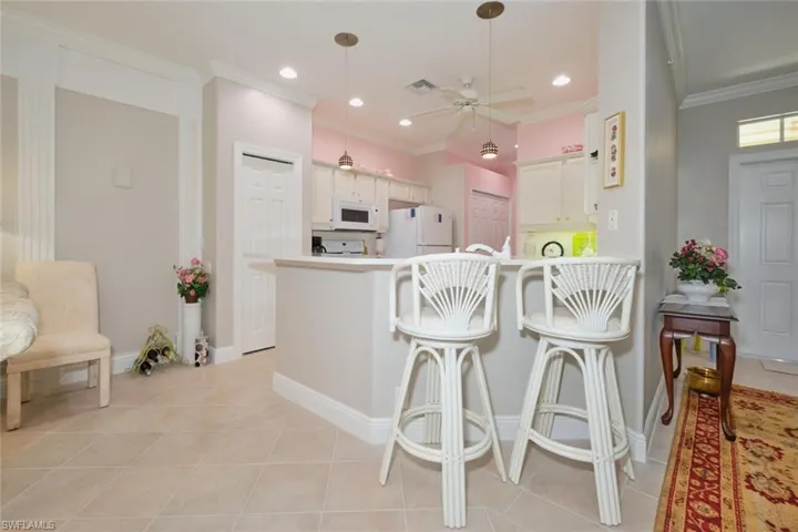 Kitchen with white cabinets, light tile patterned floors, kitchen peninsula, white appliances, and ceiling fan