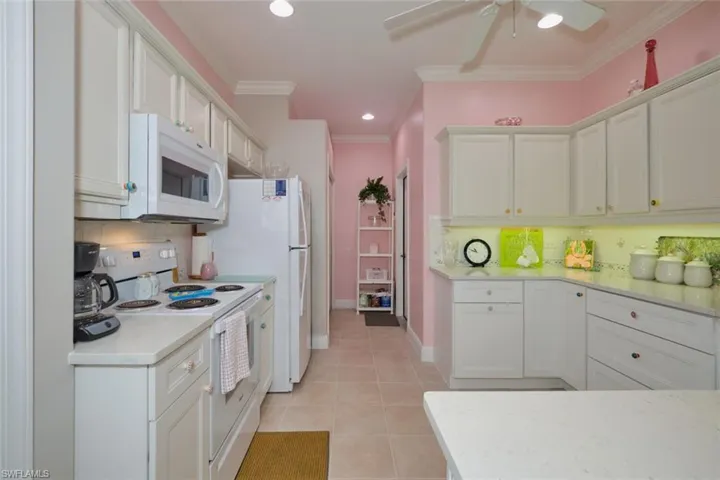 Kitchen featuring backsplash, light tile patterned floors, white appliances, ceiling fan, and white cabinets