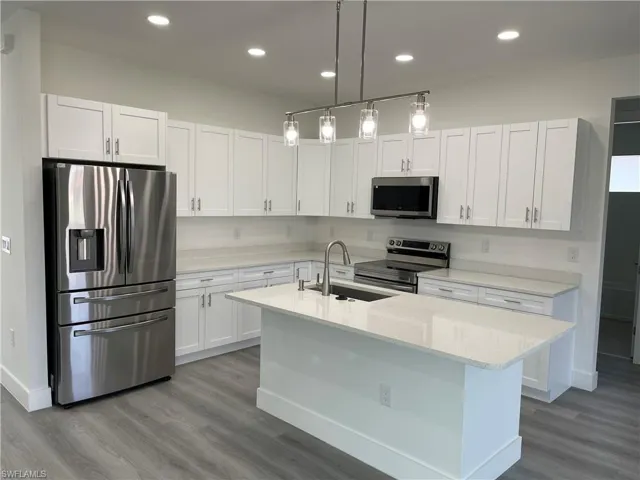 Kitchen featuring stainless steel appliances, wood finished floors, white cabinetry, a kitchen island with sink, and recessed lighting