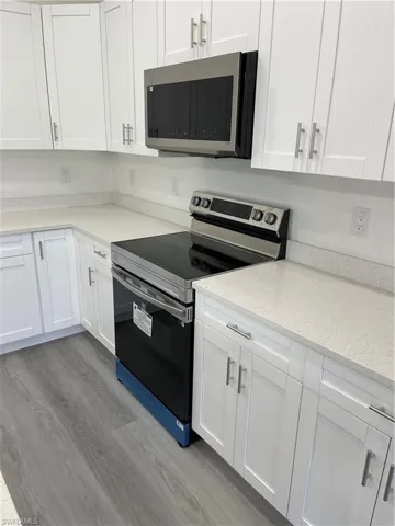 Kitchen featuring stainless steel range with electric stovetop, light wood-style floors, white cabinetry, and light stone counters
