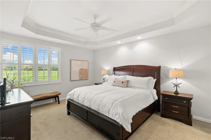 Bedroom featuring ornamental molding, light carpet, a ceiling fan, and a raised ceiling