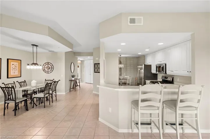 Kitchen featuring white cabinets, light tile patterned flooring, pendant lighting, a kitchen breakfast bar, and appliances with stainless steel finishes