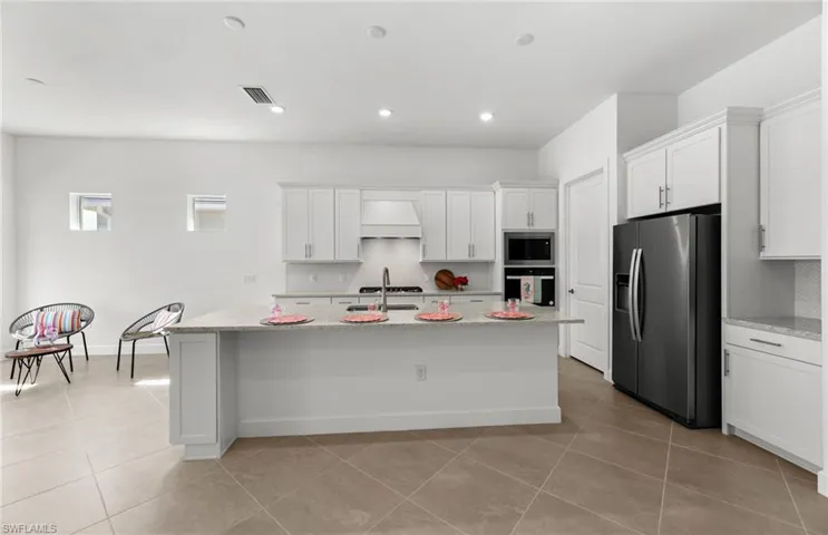 Kitchen with an island with sink, light tile floors, custom exhaust hood, and appliances with stainless steel finishes