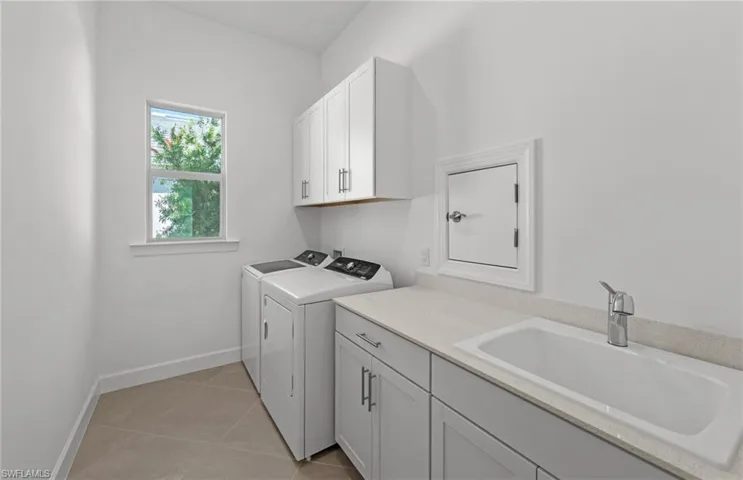 Laundry area featuring independent washer and dryer, sink, cabinets, and light tile floors