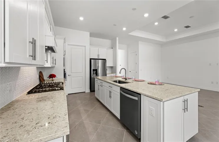 Kitchen featuring backsplash, stainless steel appliances, a raised ceiling, an island with sink, and sink