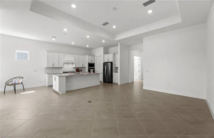 Kitchen featuring a tray ceiling, light tile floors, a kitchen island with sink, and appliances with stainless steel finishes