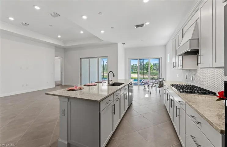 Kitchen with tasteful backsplash, a center island with sink, custom range hood, sink, and appliances with stainless steel finishes