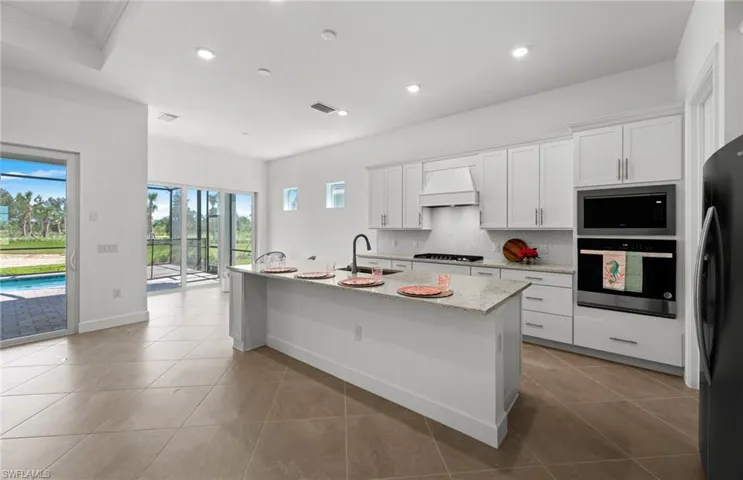 Kitchen featuring an island with sink, premium range hood, black appliances, and light tile floors